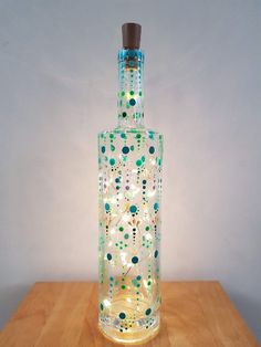 a glass bottle with lights in it on top of a wooden table next to a white wall