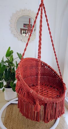 a red hanging chair with tassels on the bottom and side, next to a potted plant