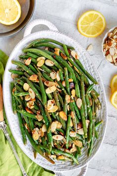 green beans and almonds in a white serving dish next to sliced lemons on a table