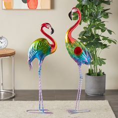 two colorful flamingos standing next to each other in front of a potted plant