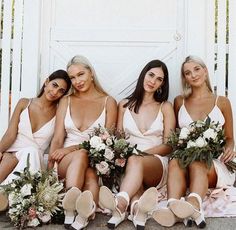 four bridesmaids in white dresses are sitting on the steps with their bouquets