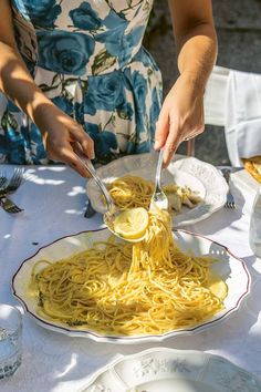 a woman is spooning noodles from a plate on a table with plates and silverware