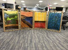 four paintings are on display in an office cubicle with chairs and desks behind them