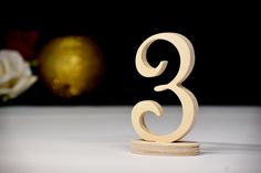 a wooden cake topper with the number three on it's stand next to a rose