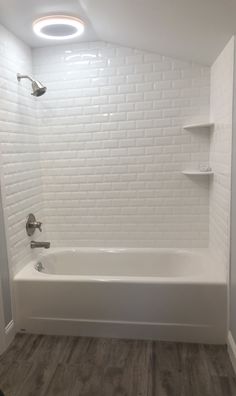 an empty bathroom with white brick walls and wood flooring, including a bathtub