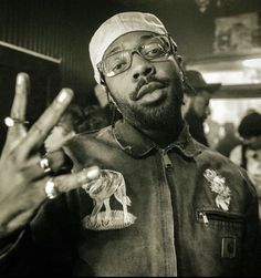 a man wearing glasses and a hat making the peace sign with his fingers in front of him