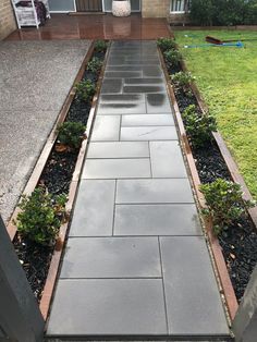 an outdoor walkway leading to a house with grass in the back ground and bushes on either side