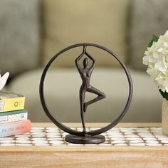 a statue of a woman doing yoga on a table next to some books and flowers