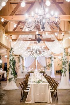 a table set up for an event with white drapes and greenery on the ceiling