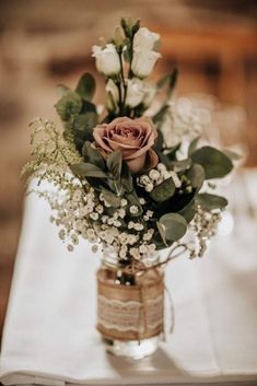 a vase filled with flowers and greenery on top of a white cloth covered table