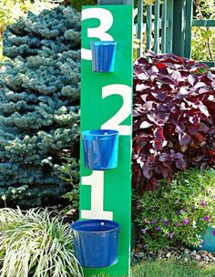 a number sign with three blue buckets on it in front of some plants and bushes