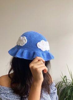 a woman wearing a blue crocheted hat with white clouds on the brim