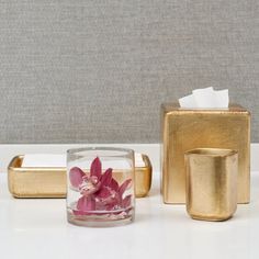 gold bathroom accessories with pink flower in glass container and tissue dispenser on counter