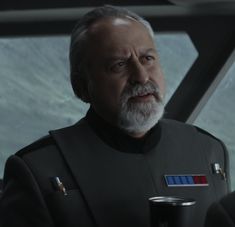 an older man with grey hair and beard wearing a star wars uniform holding a drink in his hand