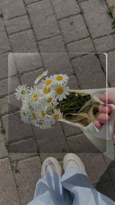 a person is holding a bouquet of daisies in front of their face while sitting on the ground