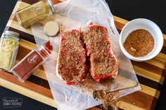 two steaks on a cutting board with spices and seasoning next to the meat