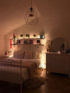 a white bed sitting under a window next to a night stand with lights on it