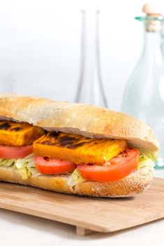 there is a sandwich that has been cut in half on a cutting board next to a bottle