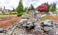 there is a small waterfall in the middle of this garden with rocks and gravel around it