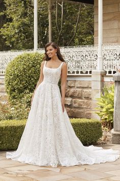 a woman in a white wedding dress standing on a stone patio with bushes behind her