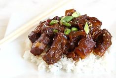 a white plate topped with meat and rice next to chopsticks on a table