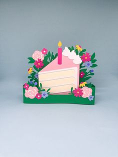 a card with a birthday cake on it and flowers around the edges that are cut out