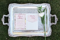 the wedding stationery was placed on an antique silver tray with a single white flower