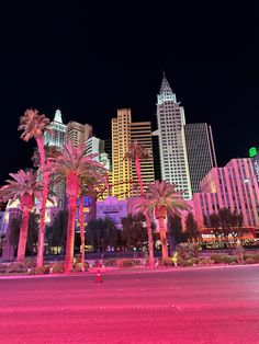 palm trees are lit up in front of the city skyline at night with pink lights