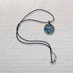 a white brick wall with a blue and green pendant on it's side hanging from a black cord