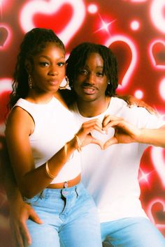 two women standing next to each other in front of a wall with hearts on it