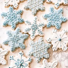 decorated cookies with blue frosting and snowflakes on top of a marble table