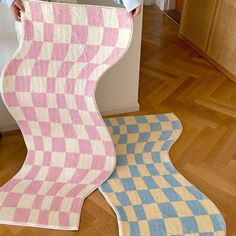 a woman holding up a pink and blue checkered rug in front of an oven