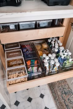 an organized kitchen drawer filled with food and drink bottles on top of a white tiled floor