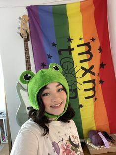 a girl wearing a frog hat in front of a rainbow flag and guitar behind her