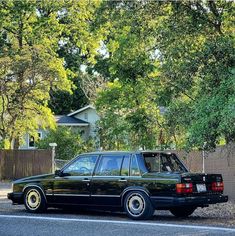 a black station wagon parked on the side of the road in front of some trees