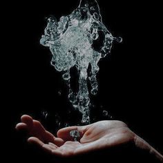 a person's hand holding water from a faucet on a black background