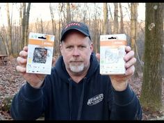 a man holding up two packages of food in front of his face with trees in the background