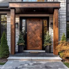 a wooden door in front of a gray brick house with potted trees on either side