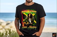 One Love Printed Bob Marley T-Shirt, Bob Marley Legend T-Shirt, Bob Marley Fan Sweatshirt, Custom Printed Shirts, One Love Unisex T-Shirt ✨Our Bob Marley "One Love" T-shirt is the ideal way to celebrate the legacy of the reggae legend. Highlighting the iconic "One Love" message, this custom-printed shirt can be personalized with your favorite colors, words, or images. Available in sizes Small to 3X, this unisex shirt is ideal for Bob Marley fans, couples, or anyone who appreciates immortal music and style. ✨Made using a commercial-grade DTG printer, each Bob Marley Legend shirt is pretreated and lint-rolled for a graceful, high-quality finish. Choose from colors like white, green, mint green, and tan to make this shirt personal yours. Features: ⦿ Customizable with colors, words, or images. Bob Marley One Love, Bob Marley Legend, Bob Marley T Shirts, Love Message, Custom Printed Shirts, One Love, Love T Shirt, Bob Marley, Love Design