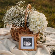 a basket filled with white flowers sitting on top of a blanket next to a photo frame