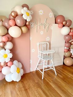 a room decorated with balloons, flowers and a chair in front of the wall that says happy