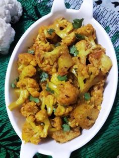 a white bowl filled with cauliflower on top of a green and black table cloth