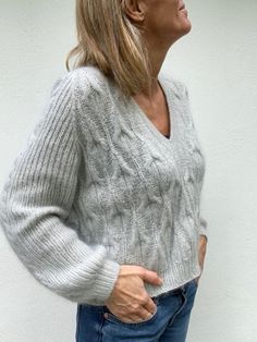 a woman standing in front of a white wall with her hand on her hip and looking up