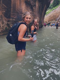 two girls are standing in the water with backpacks