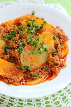 a white plate topped with pasta and meat covered in sauce on top of a green table cloth