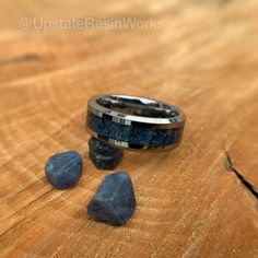 two wedding bands sitting on top of a wooden table next to some rocks and stones