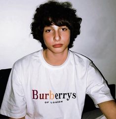 a young man wearing a burberryss t - shirt sitting on a bed