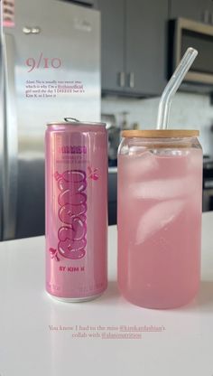 a pink drink with a straw in it next to a can of soda on a counter