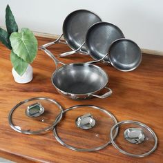 a wooden table topped with metal pots and pans next to a plant on top of it