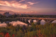 an image of a bridge that is going over the water at sunset or dawn with buildings in the background